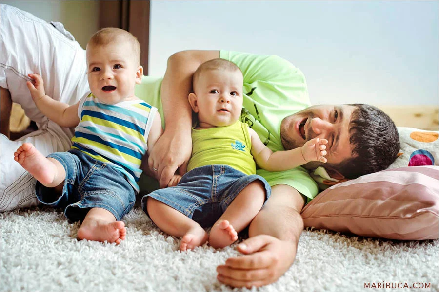 dad lies surrounded by two 8 month old twins in blue jeans