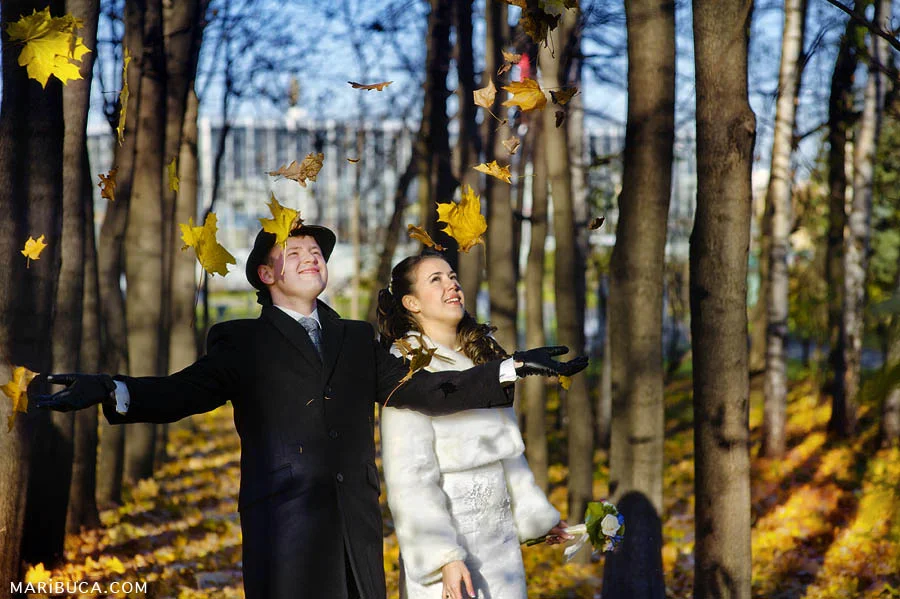 the bride and groom throw and enjoy falling yellow leaves surrounded by alleys of trees