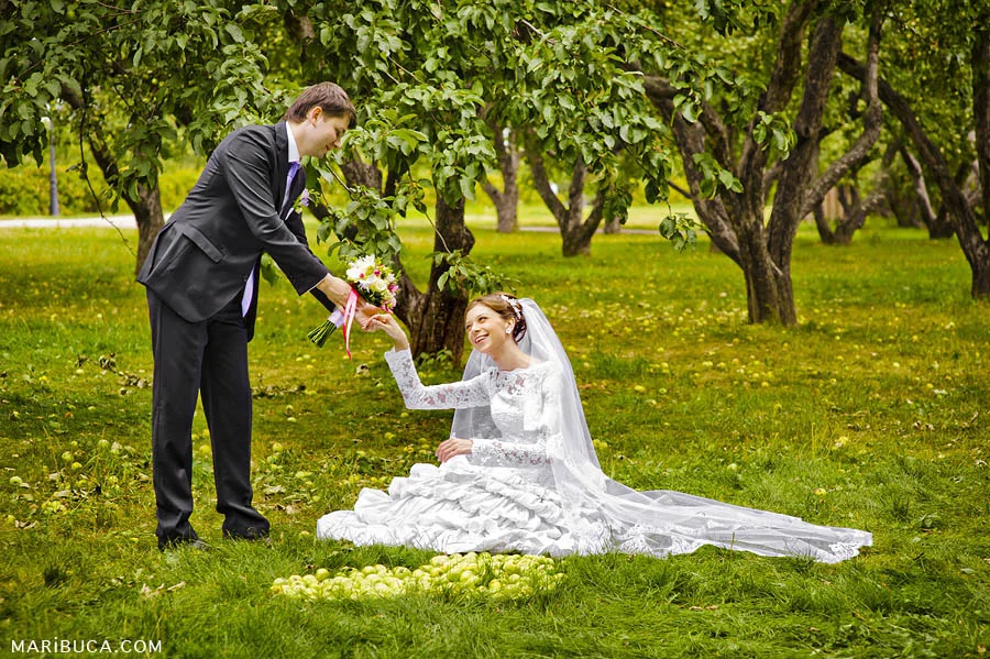 The groom and the bride are laughing in an apples orchard garden