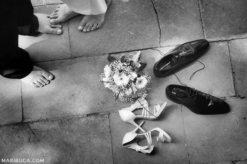 Newlyweds with bare feet and wedding bouquet and shoes lay down in the concrete.