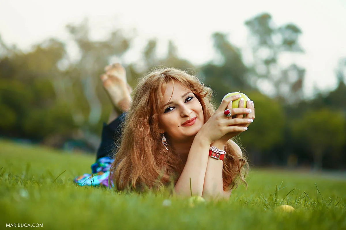 Happy girl lay downs in the green grass and holding the green apple in the Vasona Park, Los Gatos.