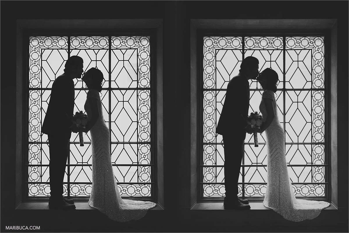 Silhouette of the bride and groom are kissing each other in front of the big window in the San Francisco City Hall.
