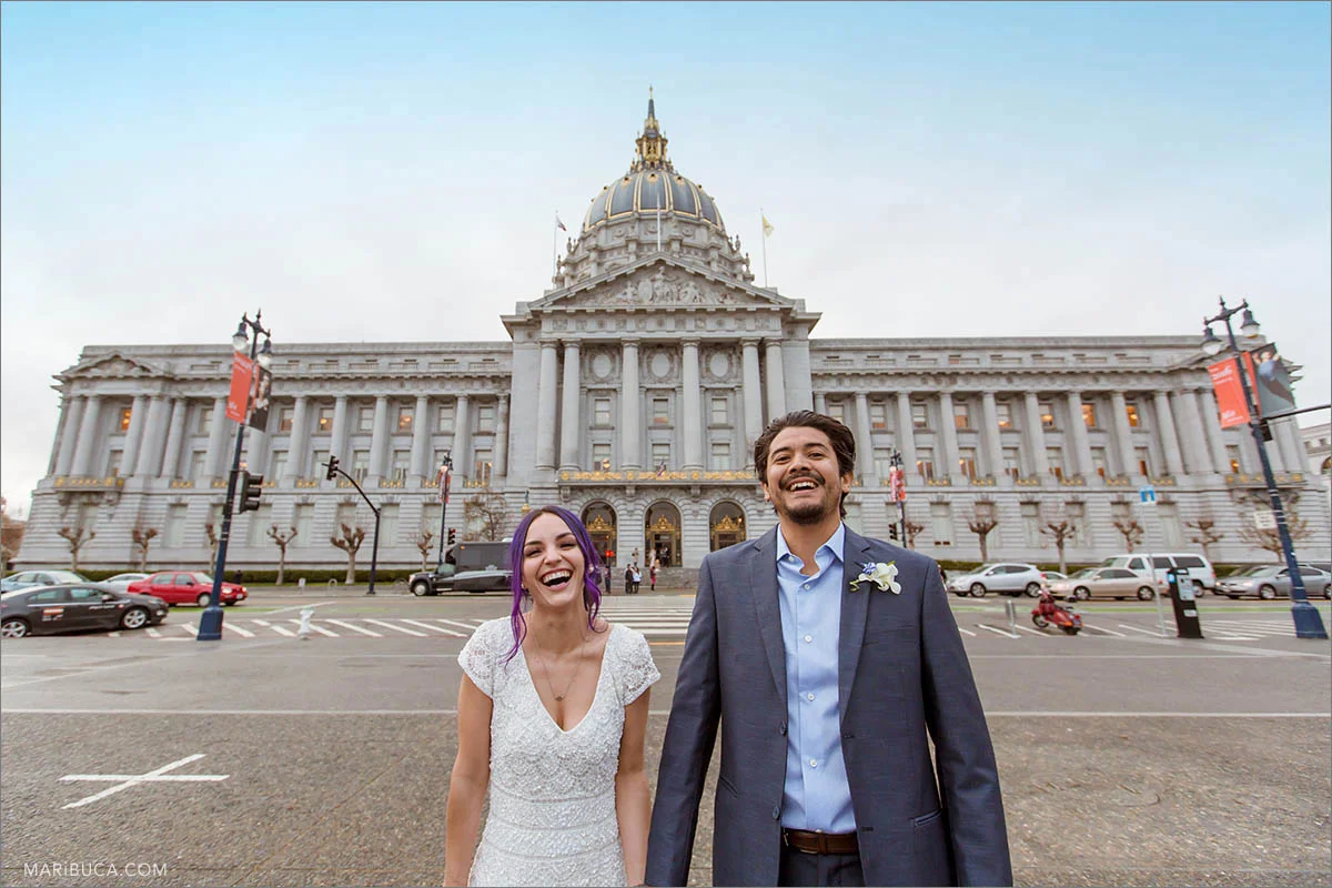 The bride and groom are laughing in the background of the San Francisco City Hall, California.