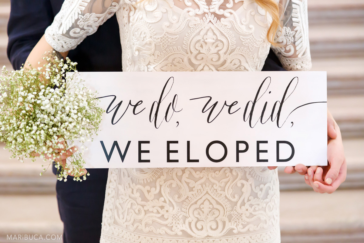 The groom and the bride show the sign “We do, we did, we Eloped”