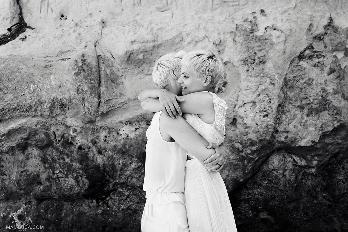 Black and white image of two brides. They hug and congrats each other after wedding ceremony in the mountain background.