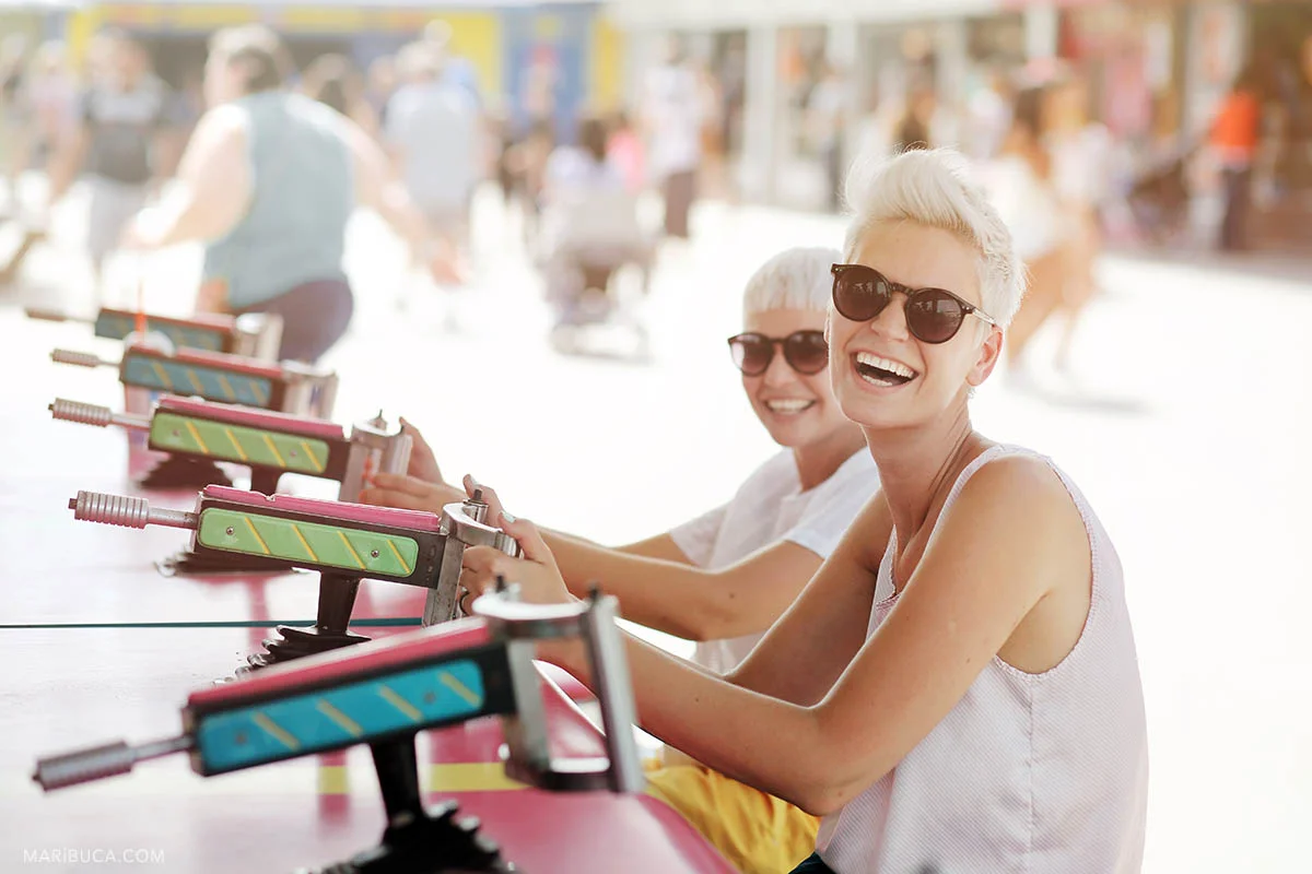 girls with short haircuts, sunglasses and white T-shirts in an amusement park are laughing, Santa Cruz.