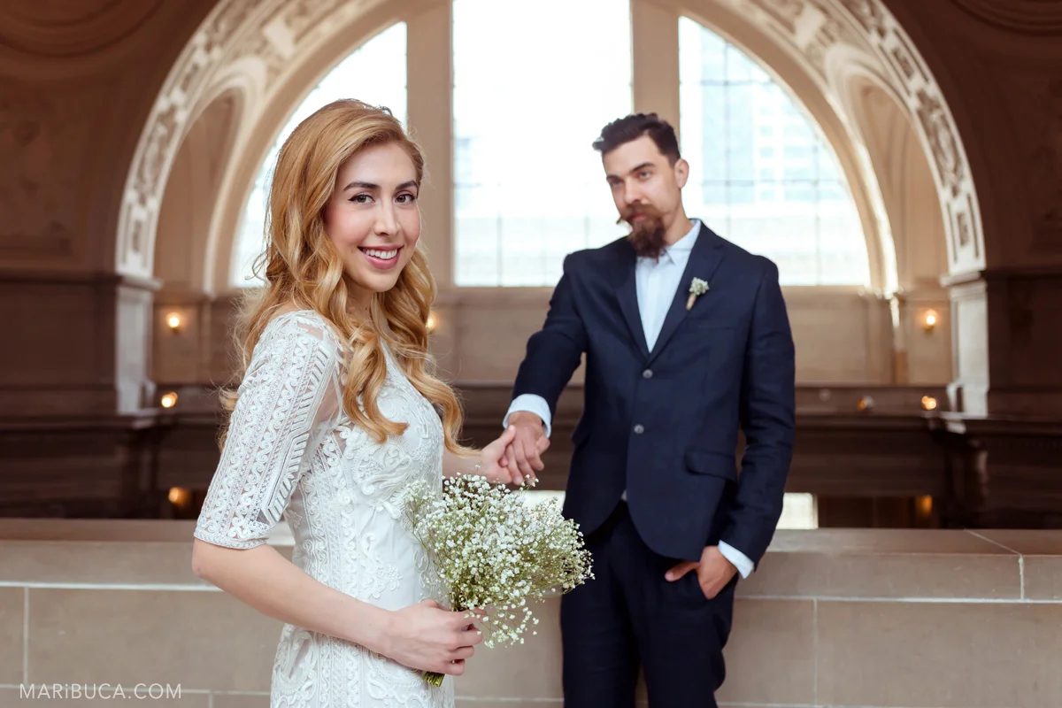 Elopement wedding and adorable couple the bride with white dress holds the groom’s hand in the fourth floor in the San Francisco City Hall.