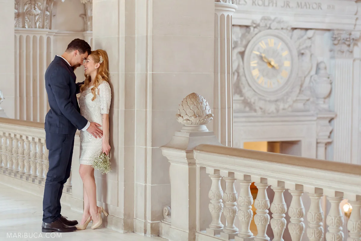 The bride and groom stand forehead to forehead and look each other indoor SF City Hall