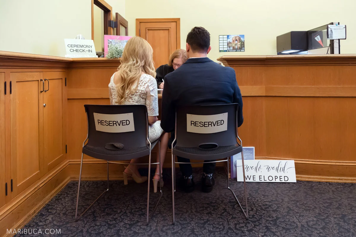before ceremony couple went to register office and sit in the black chairs with sign titles “Reserved” in san francisco city hall
