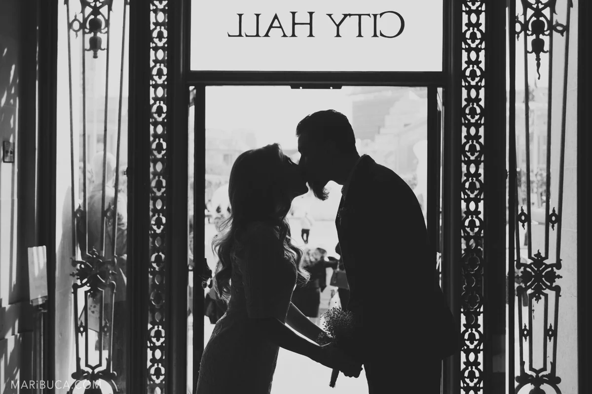 black and white image of newlyweds silhouettes with the sign City Hall in the top of the window.