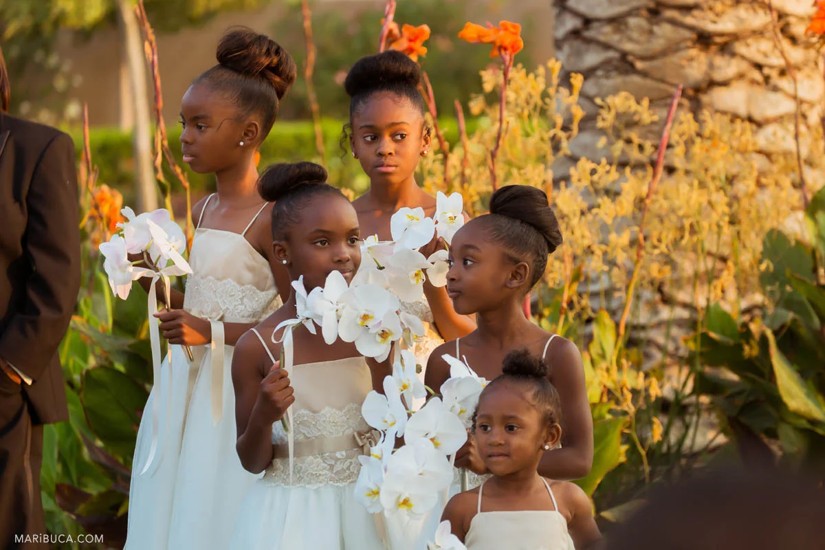 Beautiful flower girls with white dresses hold white big flowers and listen the wedding ceremony.
