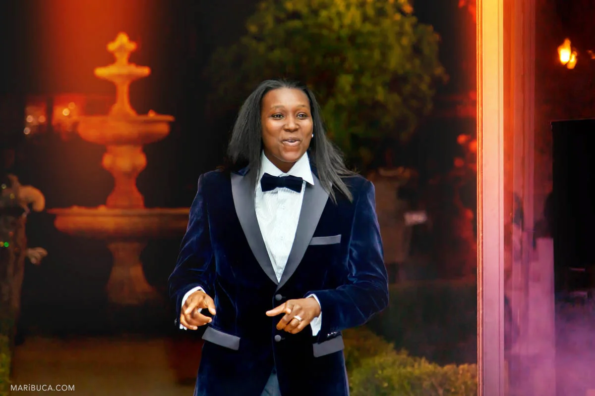 The groom is dancing coming to the reception with blue suit and the red light background in the back