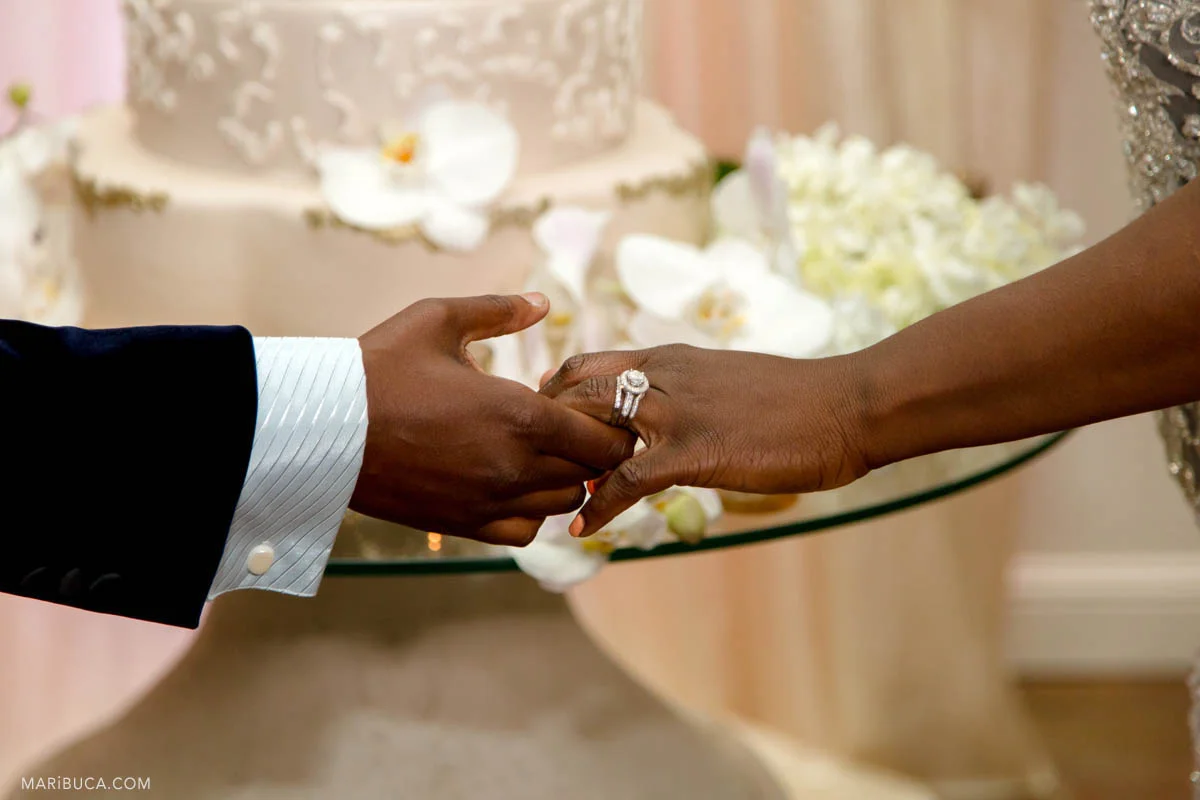 the groom and bride holding hands and the white wedding cake in the background