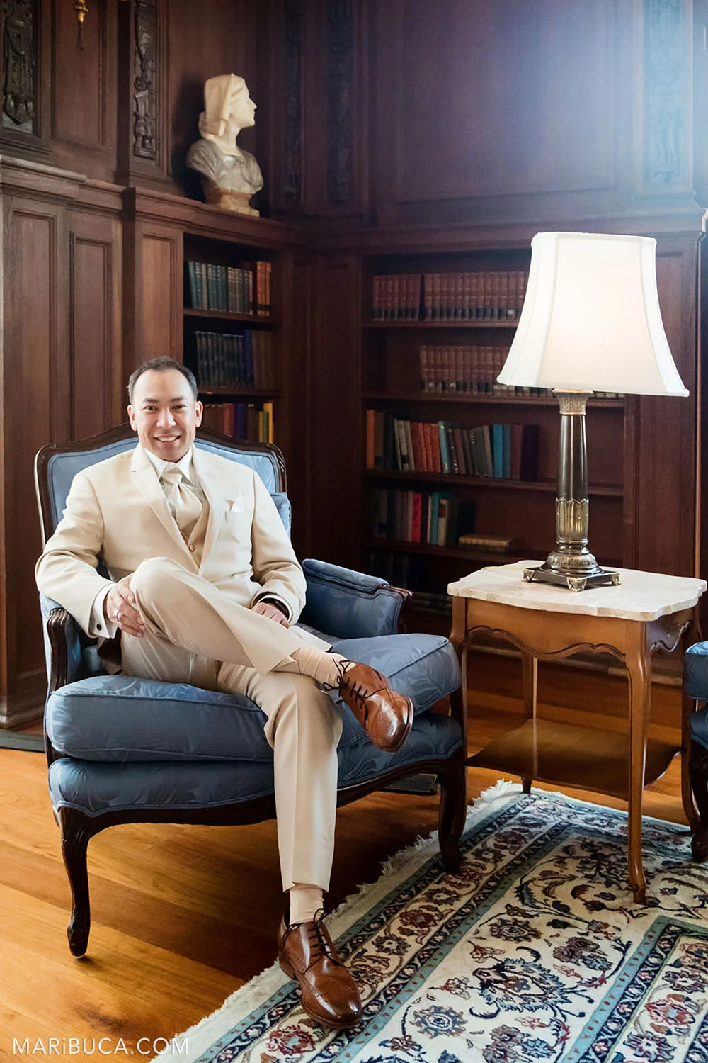 The groom smiles and sits in the Library during getting ready in the Kohl Mansion, Burlingame