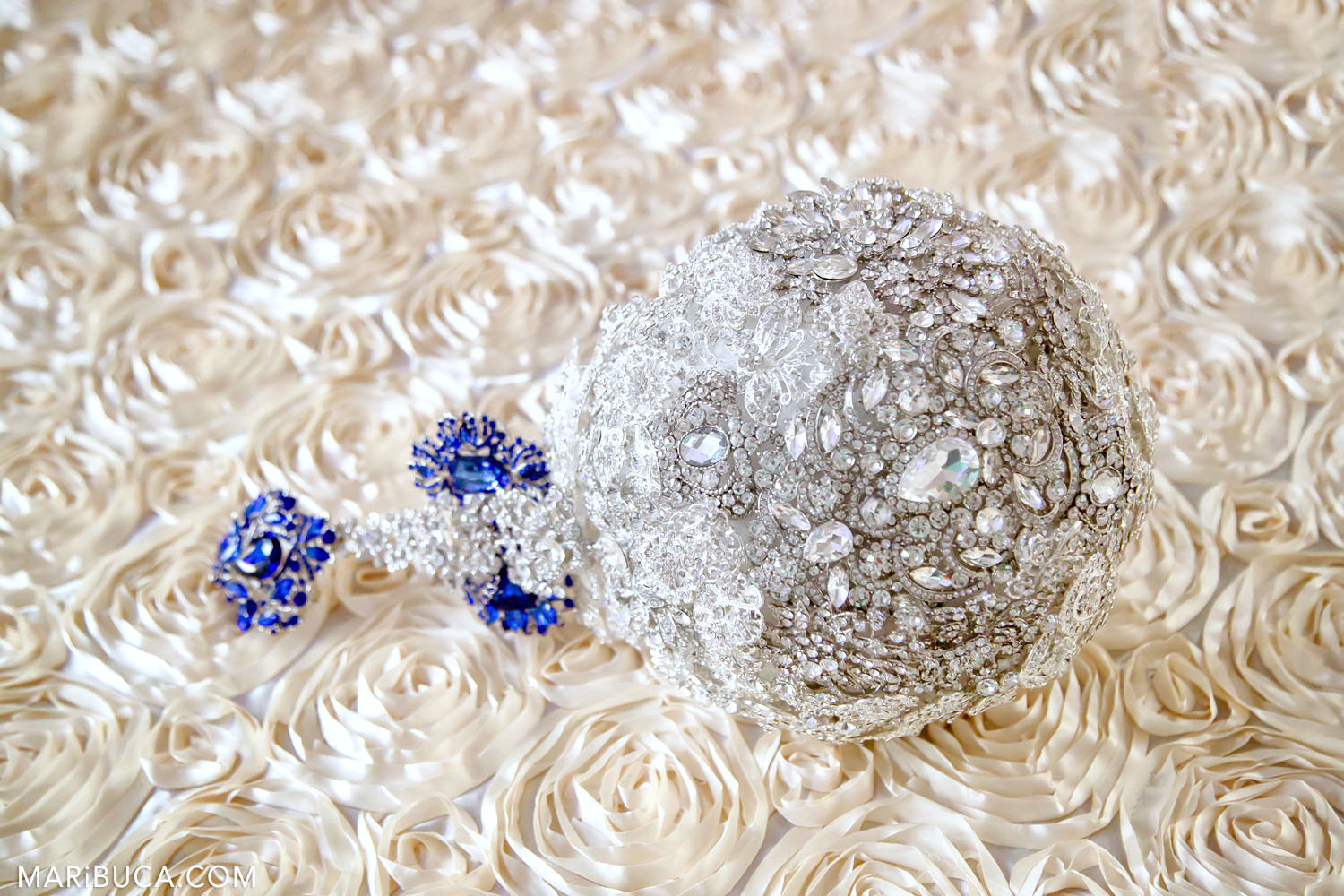 A bridal bouquet with glass and blue stones lies on a textured white tablecloth in the form of roses.