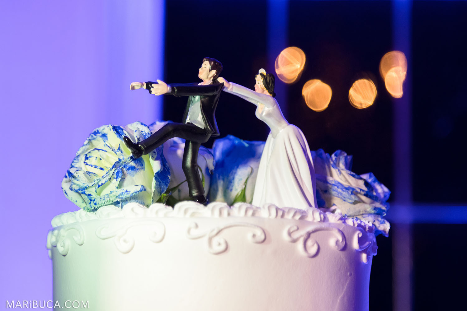 figure bride and groom on the cake: the bride is trying to keep the bride who wants to run on the background of purple and orange light bokeh.
