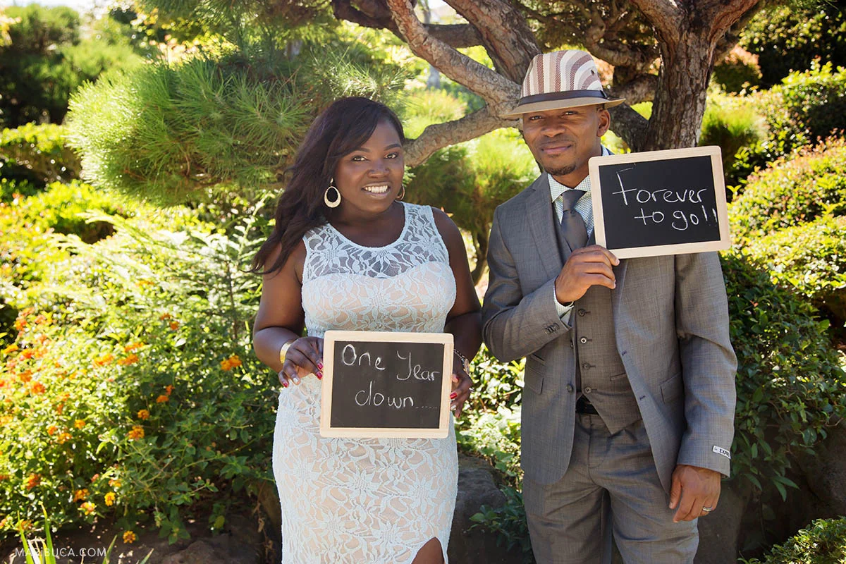 The bride holds “one year down”, the groom holds “forever to go!” chalkboard and they celebrate anniversary wedding in the Hayward Japanese Garden.
