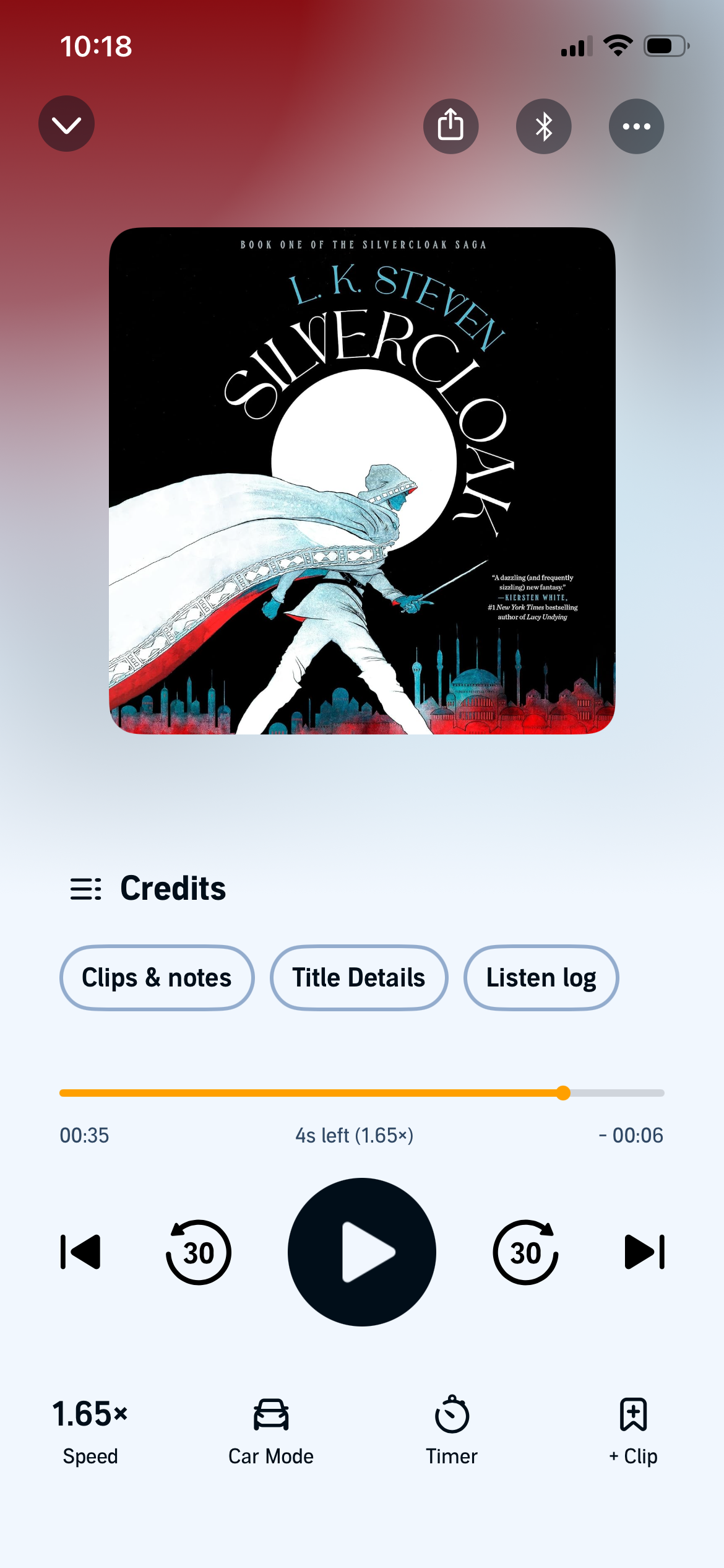 A screenshot of Silvercloak by L.K. Steven in the Audible app. The cover is mostly black with an illustration of a person in a white cloak walking through a city.