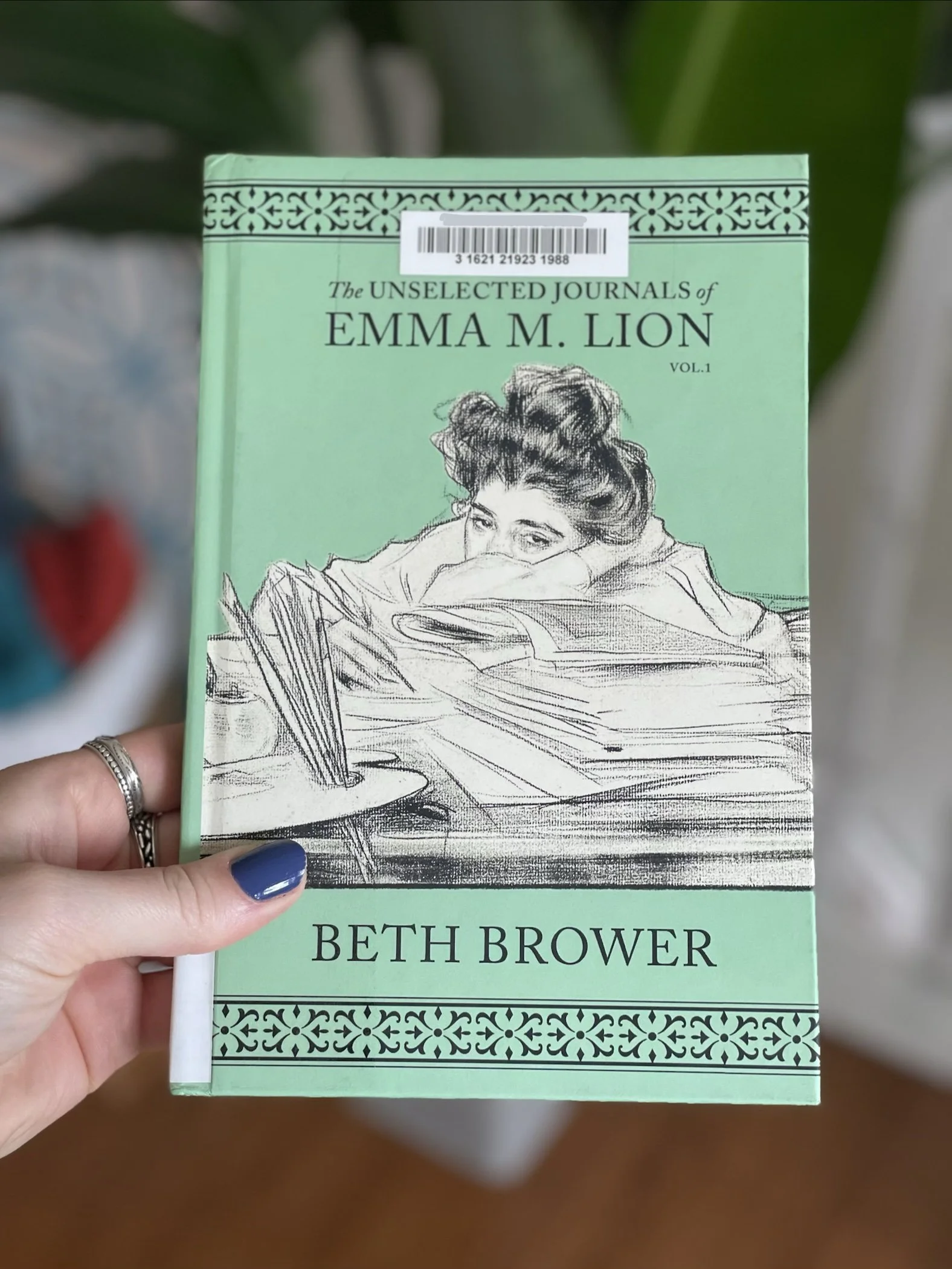 My hand holds a hard cover copy of The Unselected Journals of Emma M. Lion by Beth Brower.