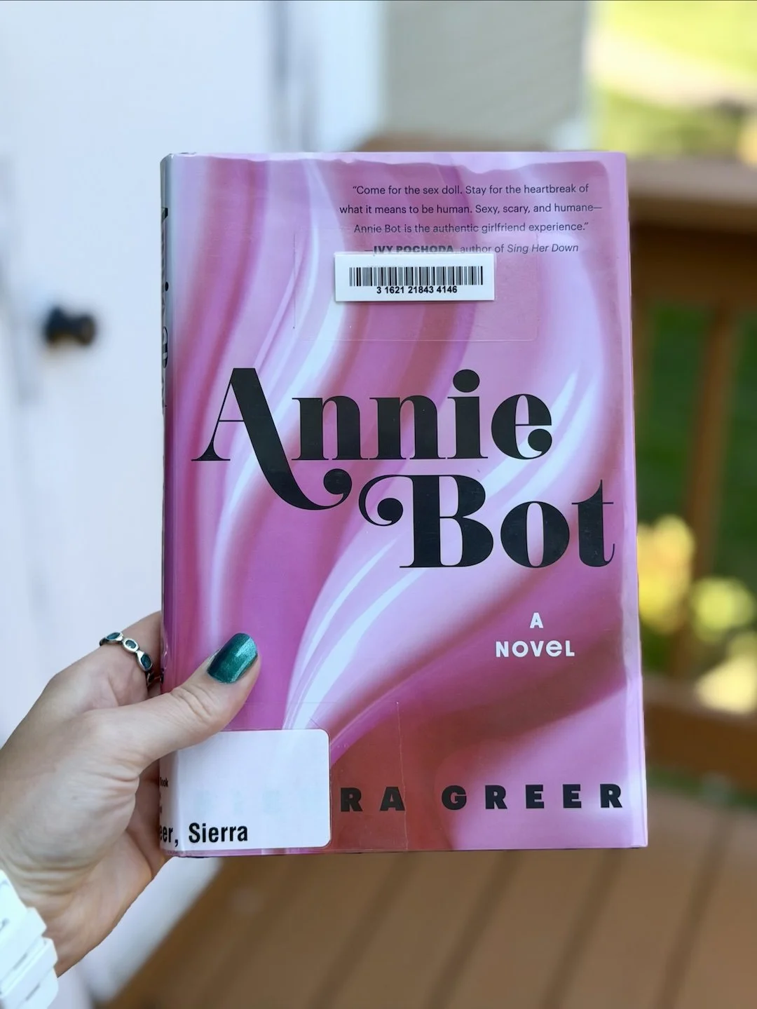My hand holds a book called Annie Bot. The cover is pink and white swirls with Annie Bot written in the center.
