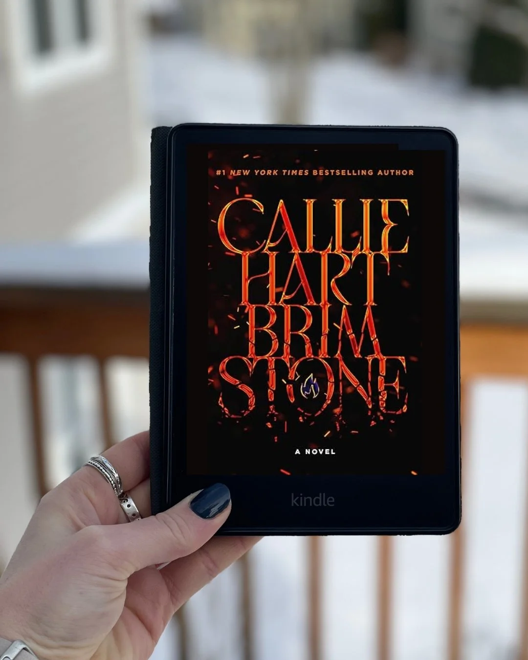 My hand holds a Kindle with Brimstone by Callie Hart on its screen. The cover is mostly black with red writing.