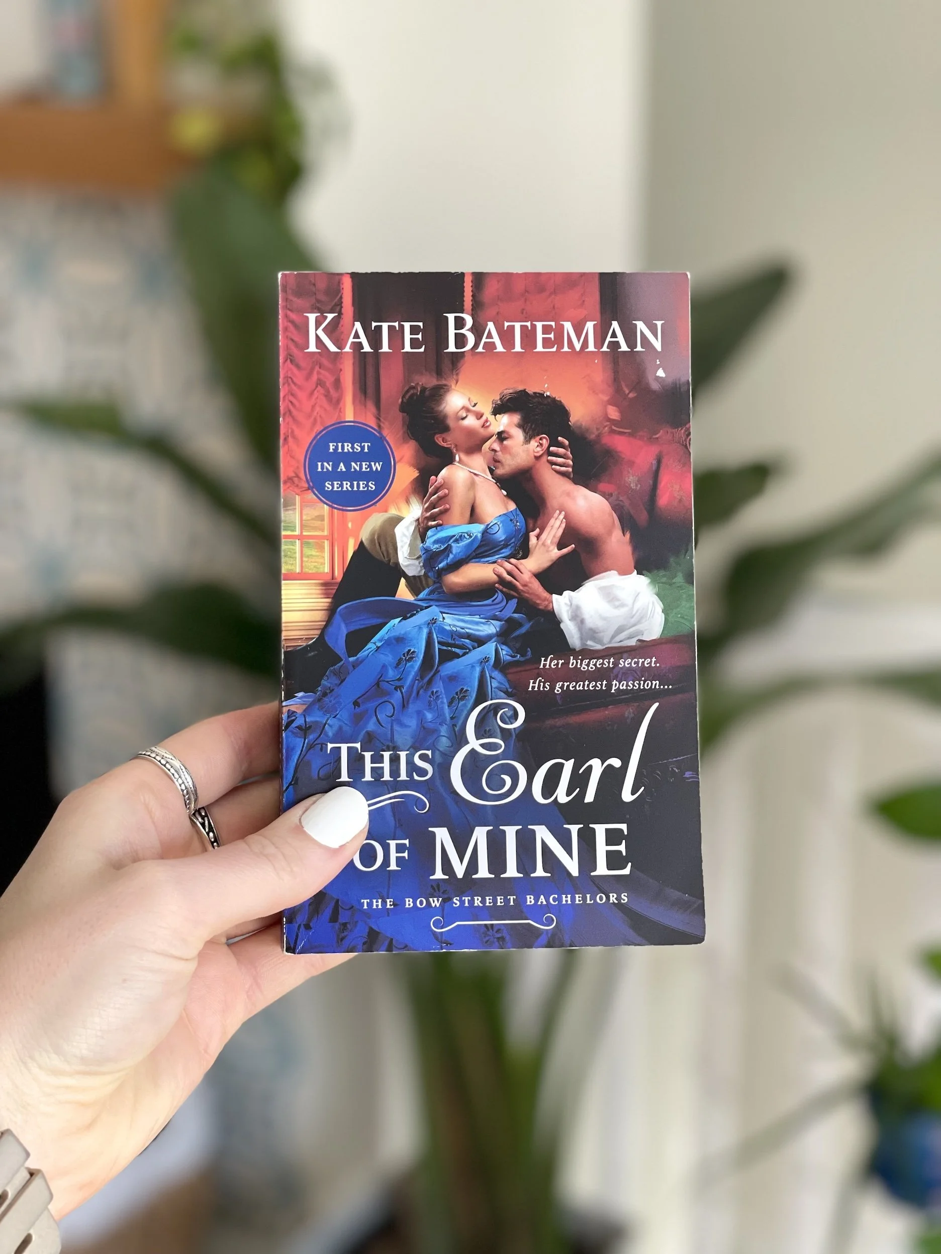 My hand holds a paperback copy of This Earl of Mine by Kate Bateman. The cover is a dramatic depiction of a man and woman holding each other.