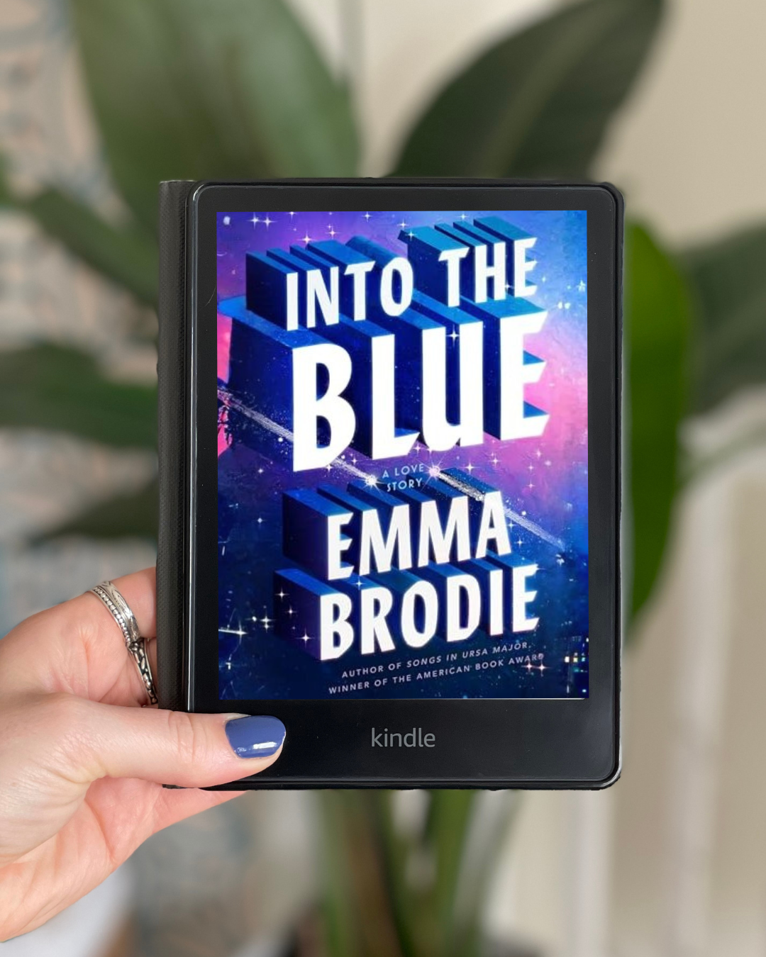 My hand holds a Kindle with Into the Blue by Emma Brodie on the screen.
