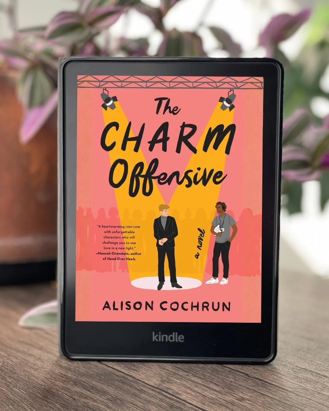 My Kindle sits on the table with the cover of The Charm Offensive by Alison Cochrun on its screen.