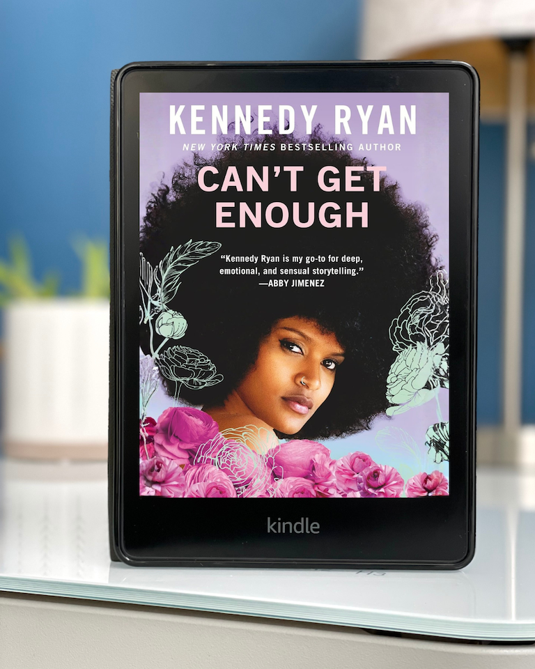 My Kindle sits on a white desk with the cover of Can't Get Enough by Kennedy Ryan on the screen. The cover is of a Black woman with an afro and nose ring surrounded by flowers.