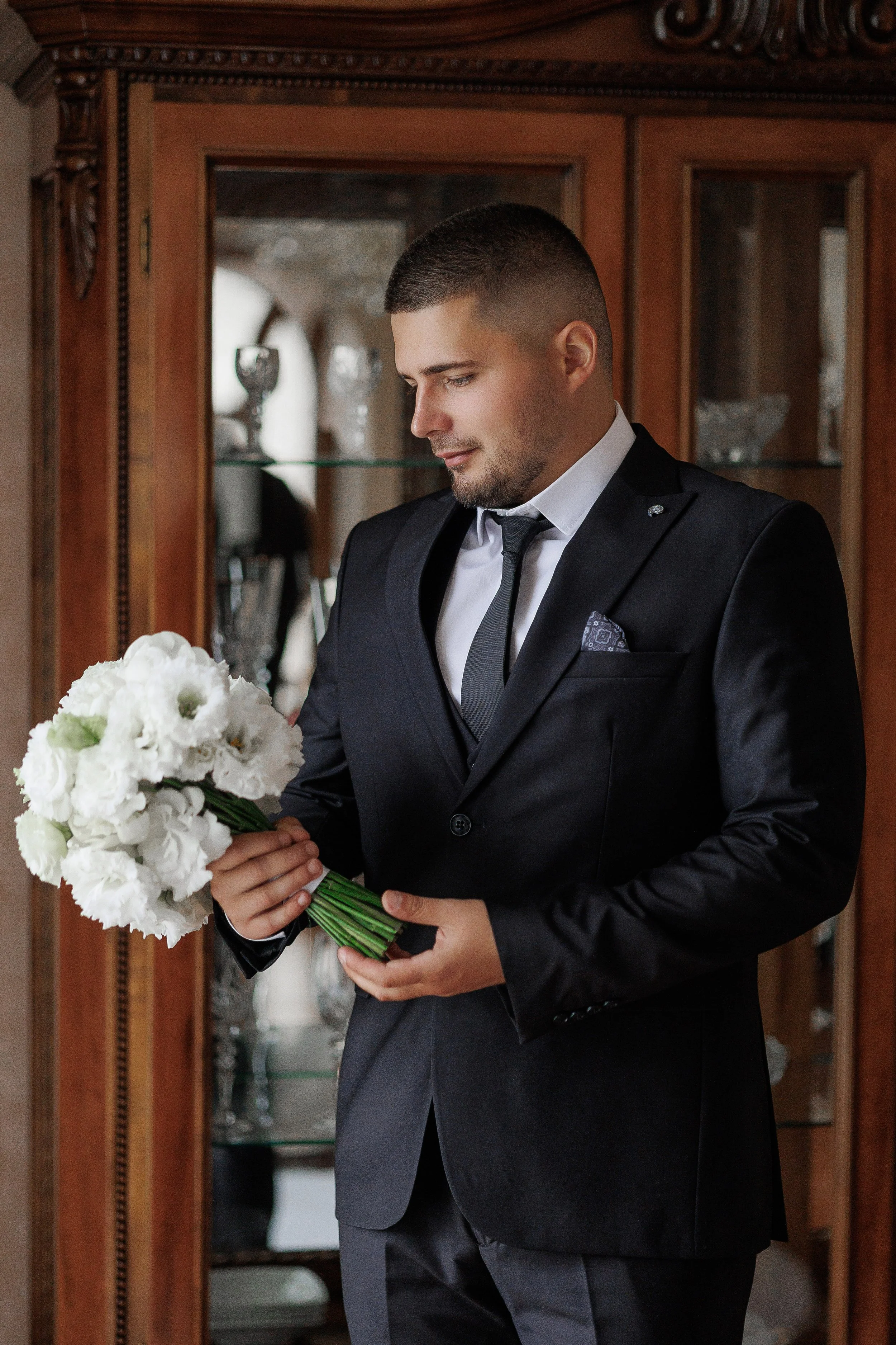 groom-formal-suit-holding-white-flower-bouquet-indoors-before-wedding-ceremony.jpg
