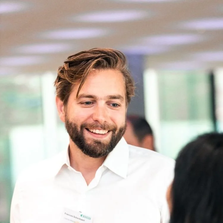 A man with a beard and styled hair smiling and looking at another person in a professional setting.