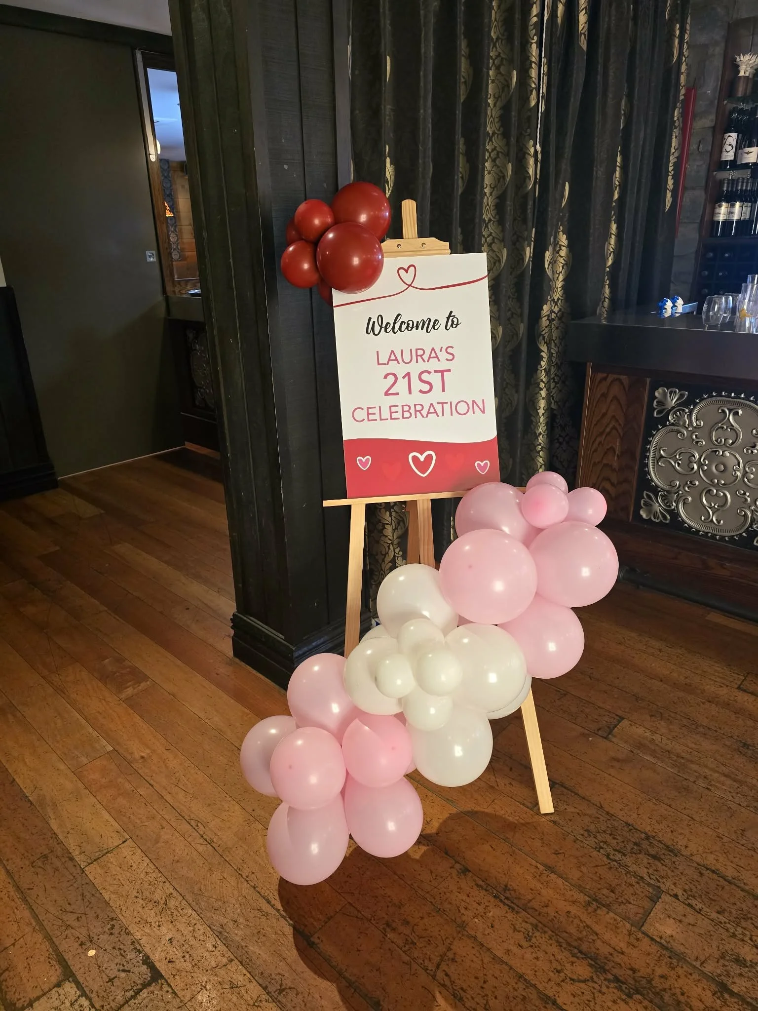 Decorative welcome sign on an easel for Laura's 21st celebration, adorned with pink, white, and red balloons.