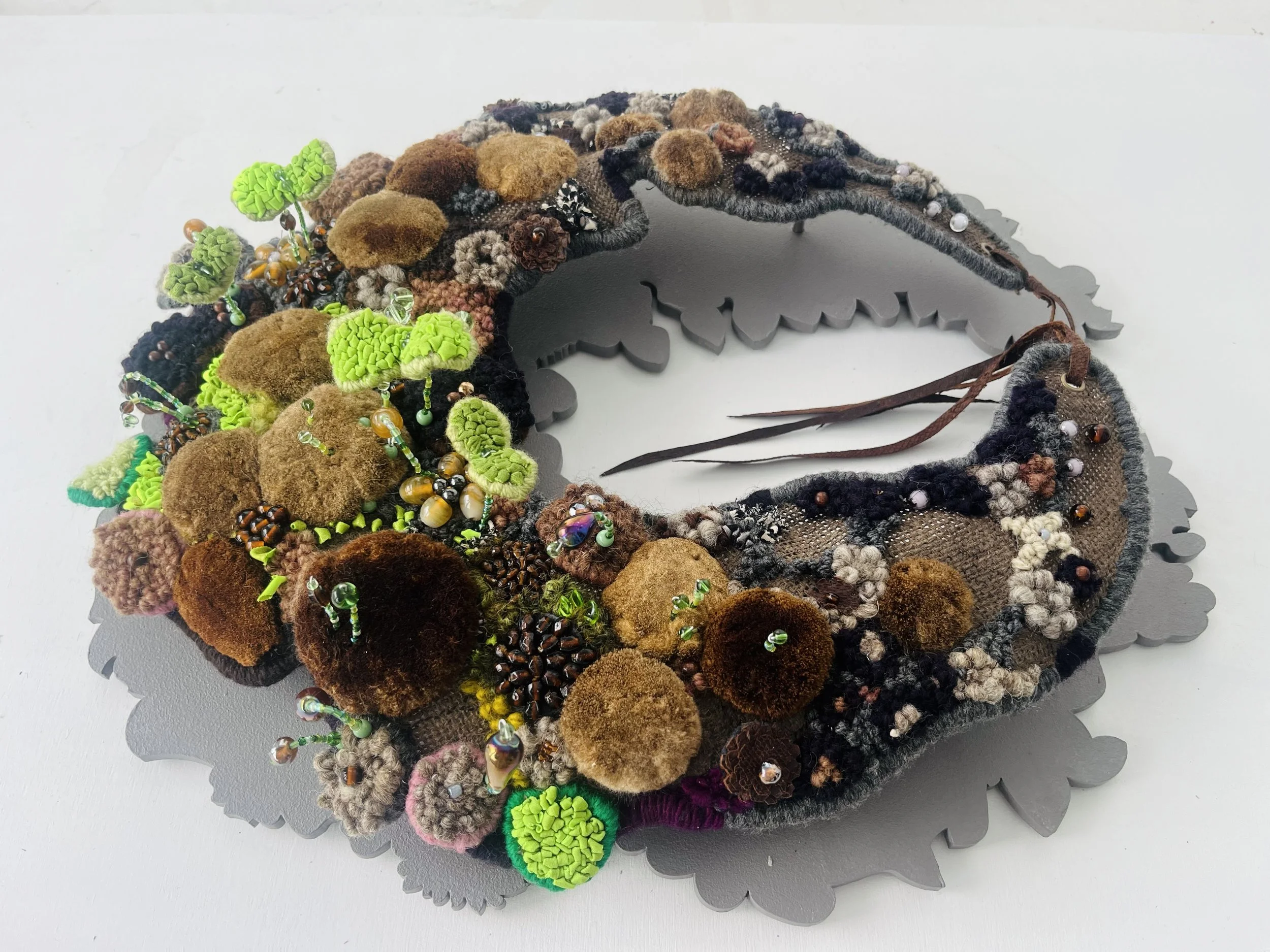 Seedwork Rising, hand hooking yarn and textiles, dyed cattail seeds, beads, fish leather, birchwood, 2026

Nineteenth-century Victorian seedwork wreaths, made from heirloom beans, squash, and grains—many now extinct—served as sentimental displays of 
