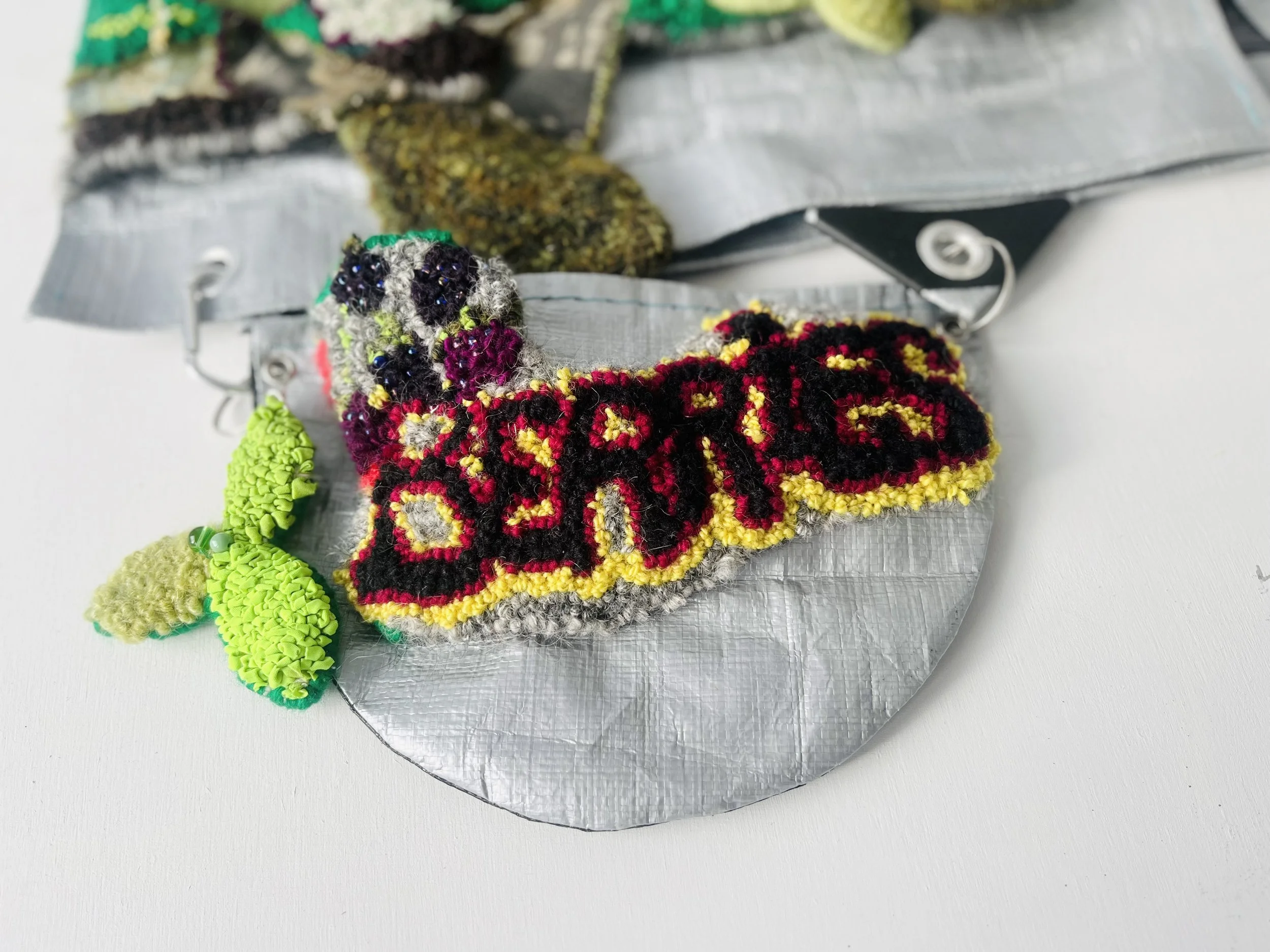 7.	Attachable Pouch, Milkweed Vest Detail, camping tarpaulin fabric, yarn, re-purposed textiles, metallic sheen textiles, beads, carabiner clip. Techniques: Hand hooked, hand beaded, machine and hand sewn, 2026