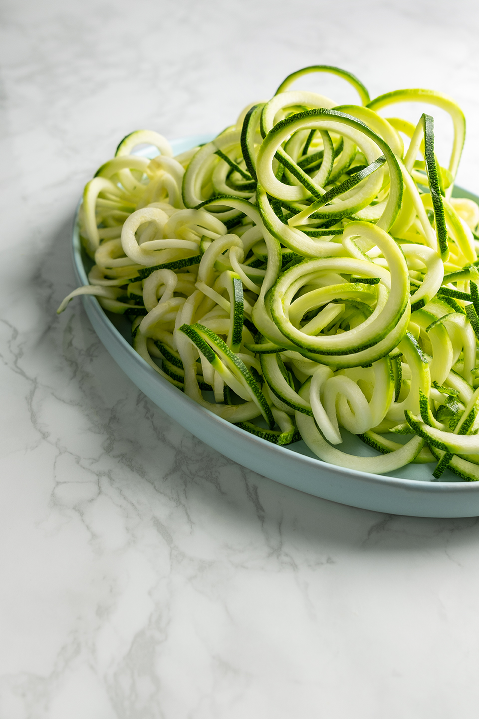  Zoodled zucchini in a pile on oval blue serving tray on a marble background.  