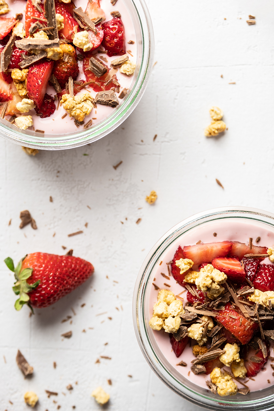  Creamy strawberry and greek yogurt with granola, sliced strawberries and shaved chocolate on textured white background. 