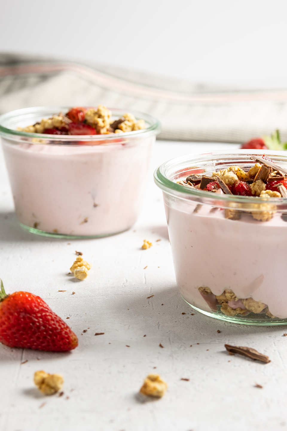  Two strawberry parfait and greek yogurt with granola, strawberries and shaved chocolate on textured white background. 