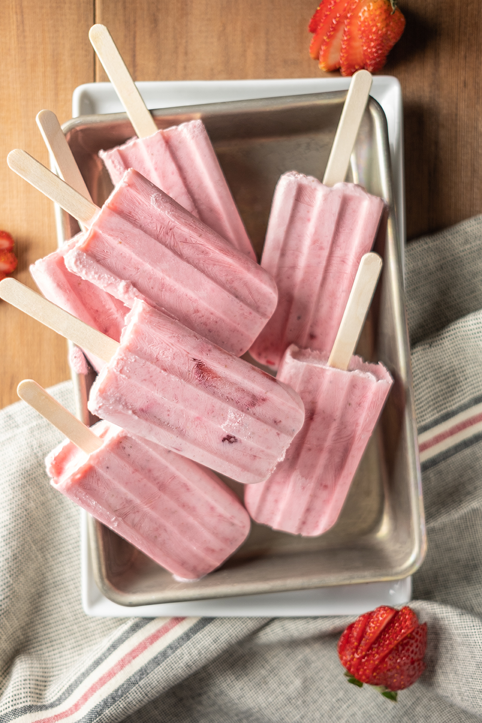  Creamy strawberry and greek yogurt popsicles in a small metal pan on a wooded background.  Shot from above. 