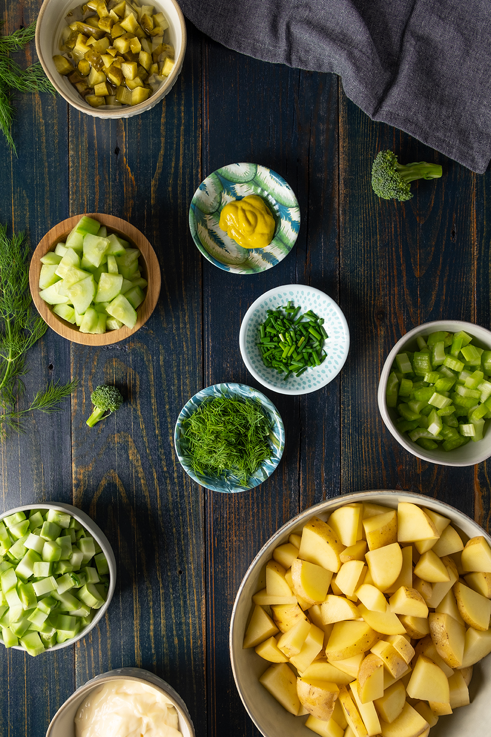  Cubed potatoes, celery, broccoli stems, dill, cucumber, mustard, chive and pickles on a rustic blue wooded background.  Navy napkin. 