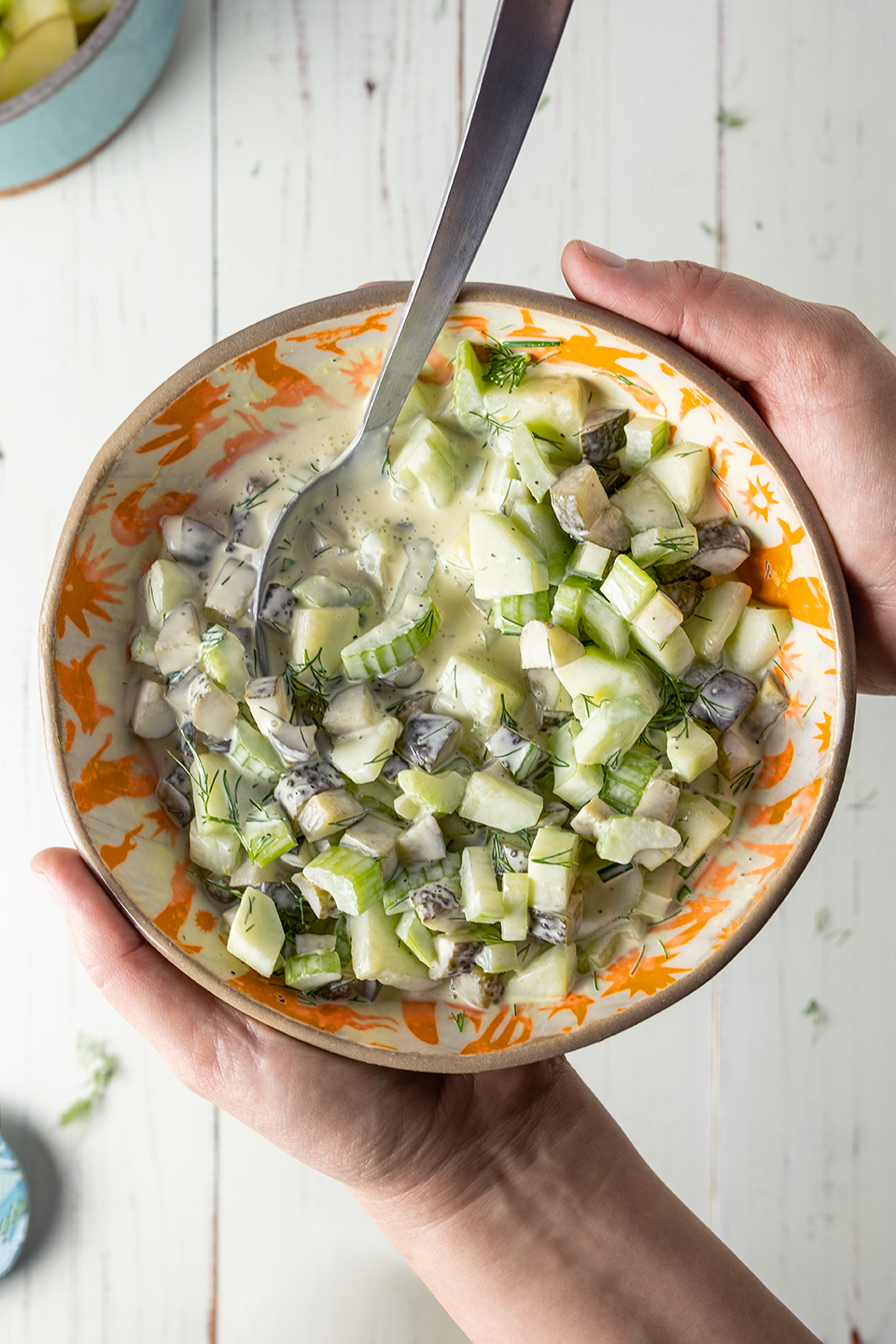  Mixture of dressing ingredients in a orange bowl being help above rustic white wooden background.  Female hands. 