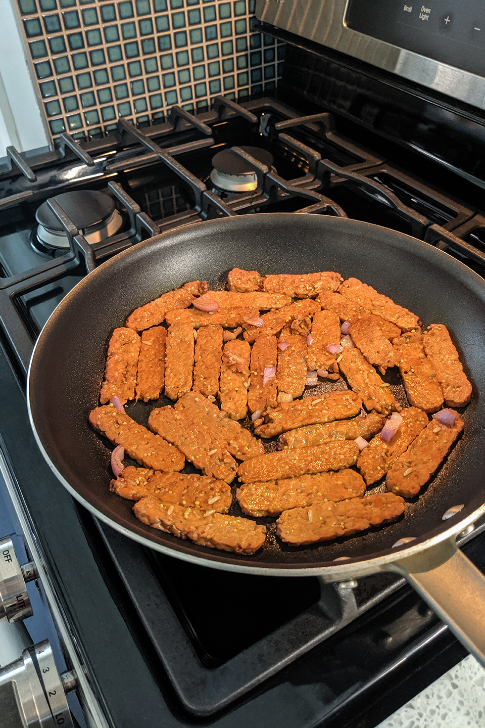  Tempeh being cooked in a large skillet on a stove.  
