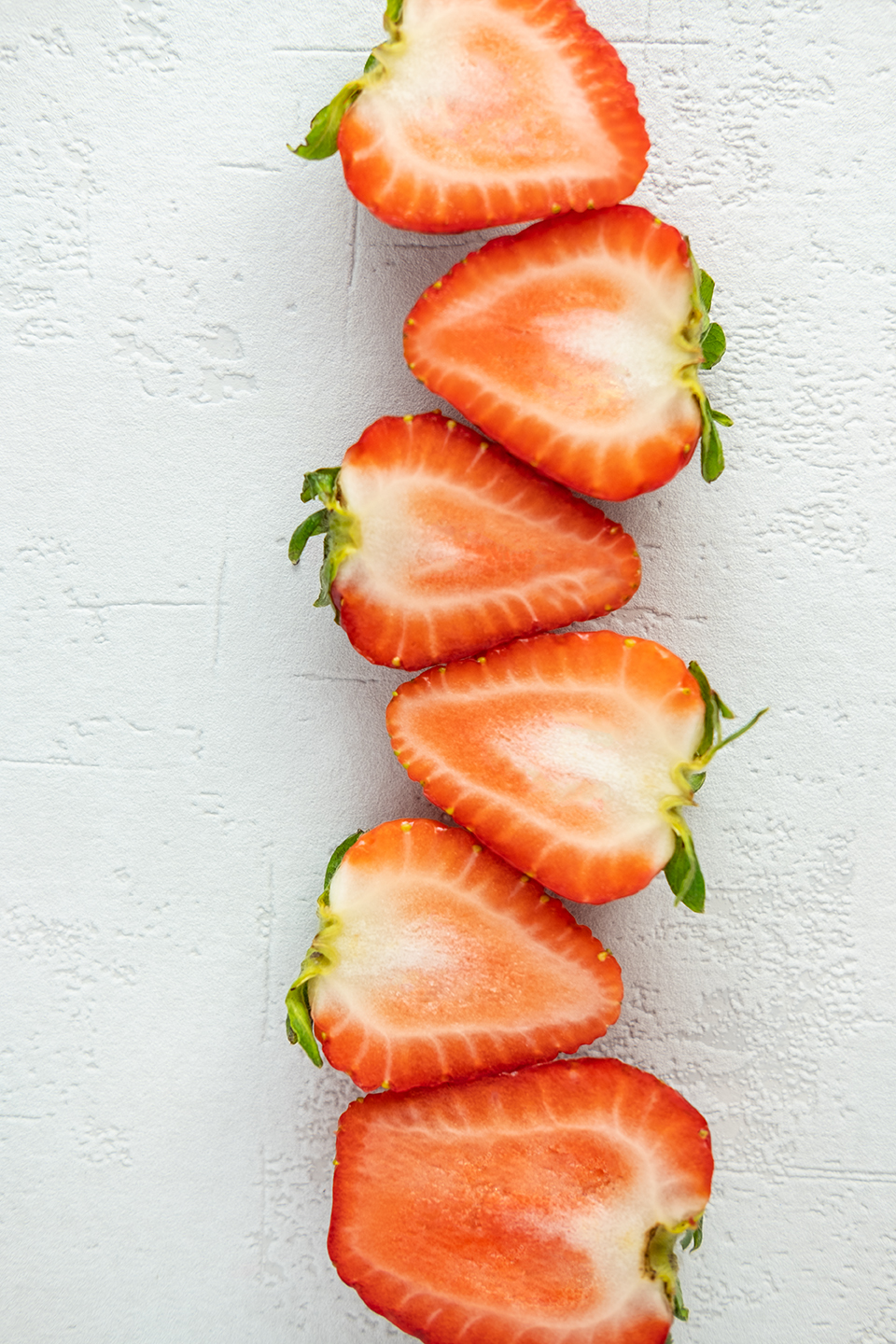  Six strawberries sliced in half on a white background. 