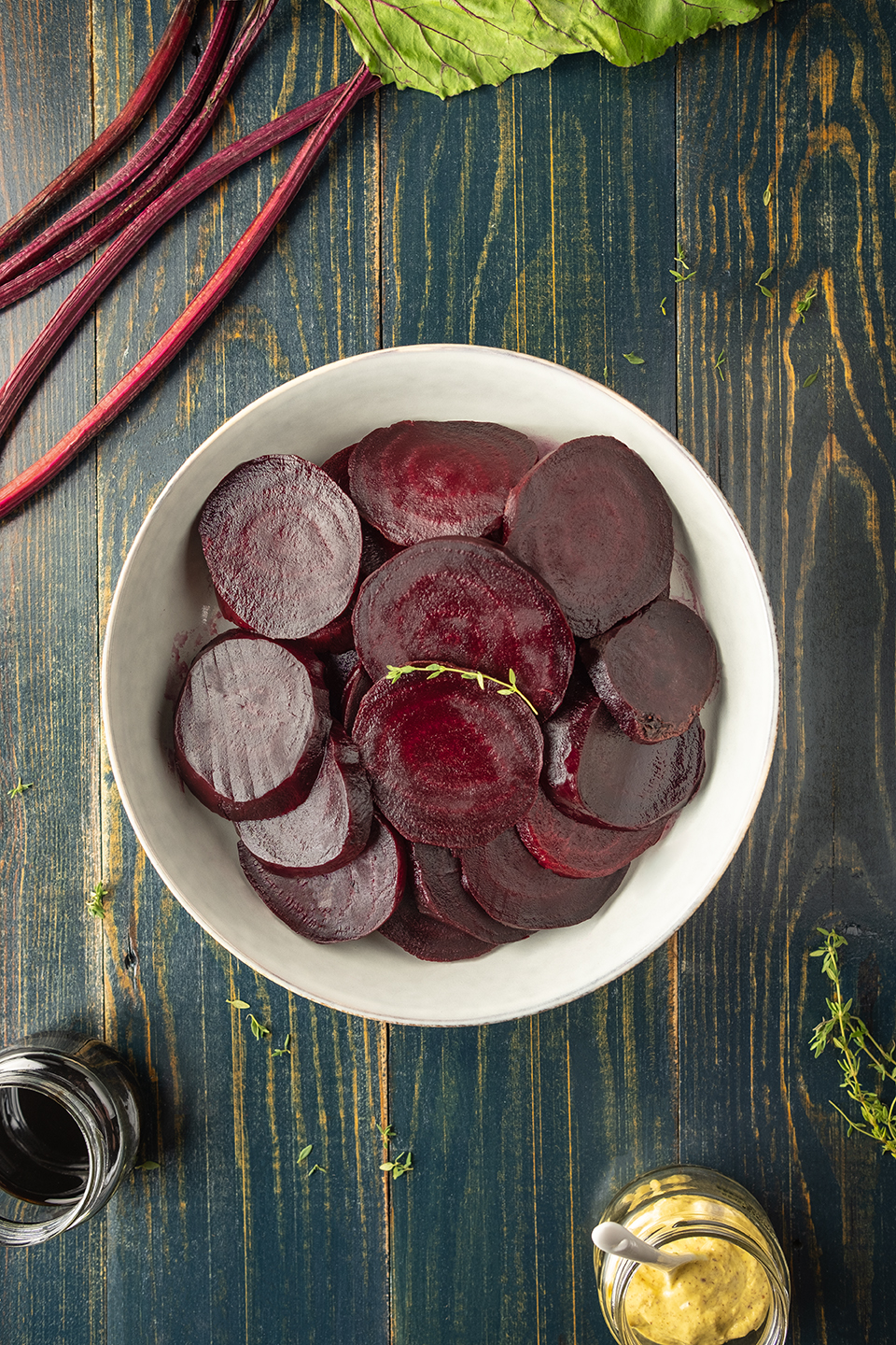  Sliced roasted beets in a grey bowl on a blue background with beet leaves and thyme.  