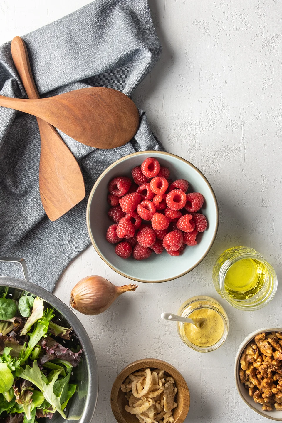  Blue bowl with raspberries, washed lettuce, shallot, crispy onions and mustard with a blue napkin on a white background.  
