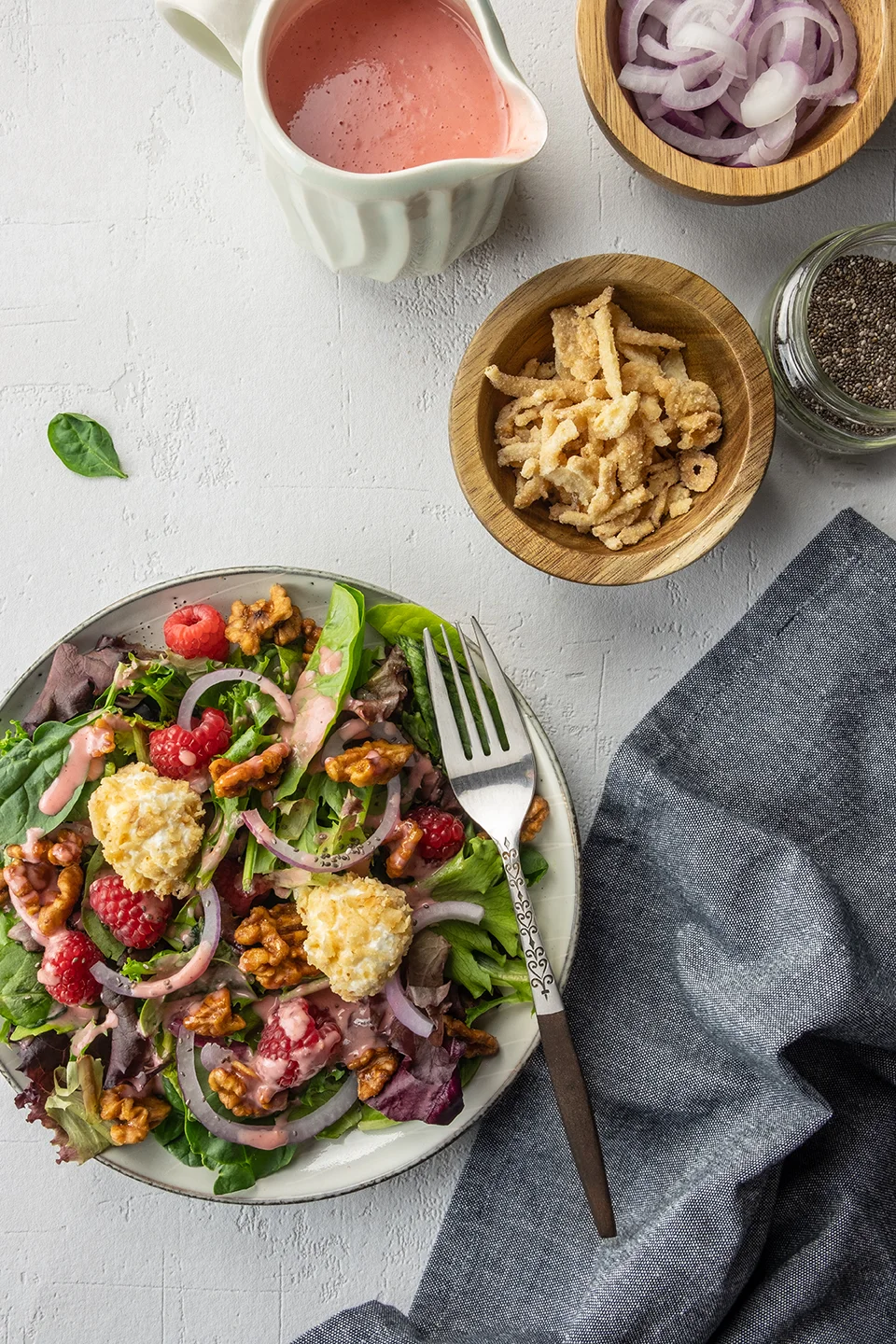  One small salad bowl with summer salad with raspberry lambic dressing.  Small bowl of crispy onions, fresh onion and dressing on white background. 