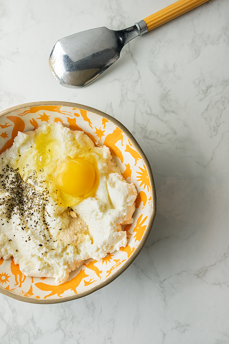  Orange bowl with fat free ricotta, egg and seasoning on a marble background with vintage spoon.  