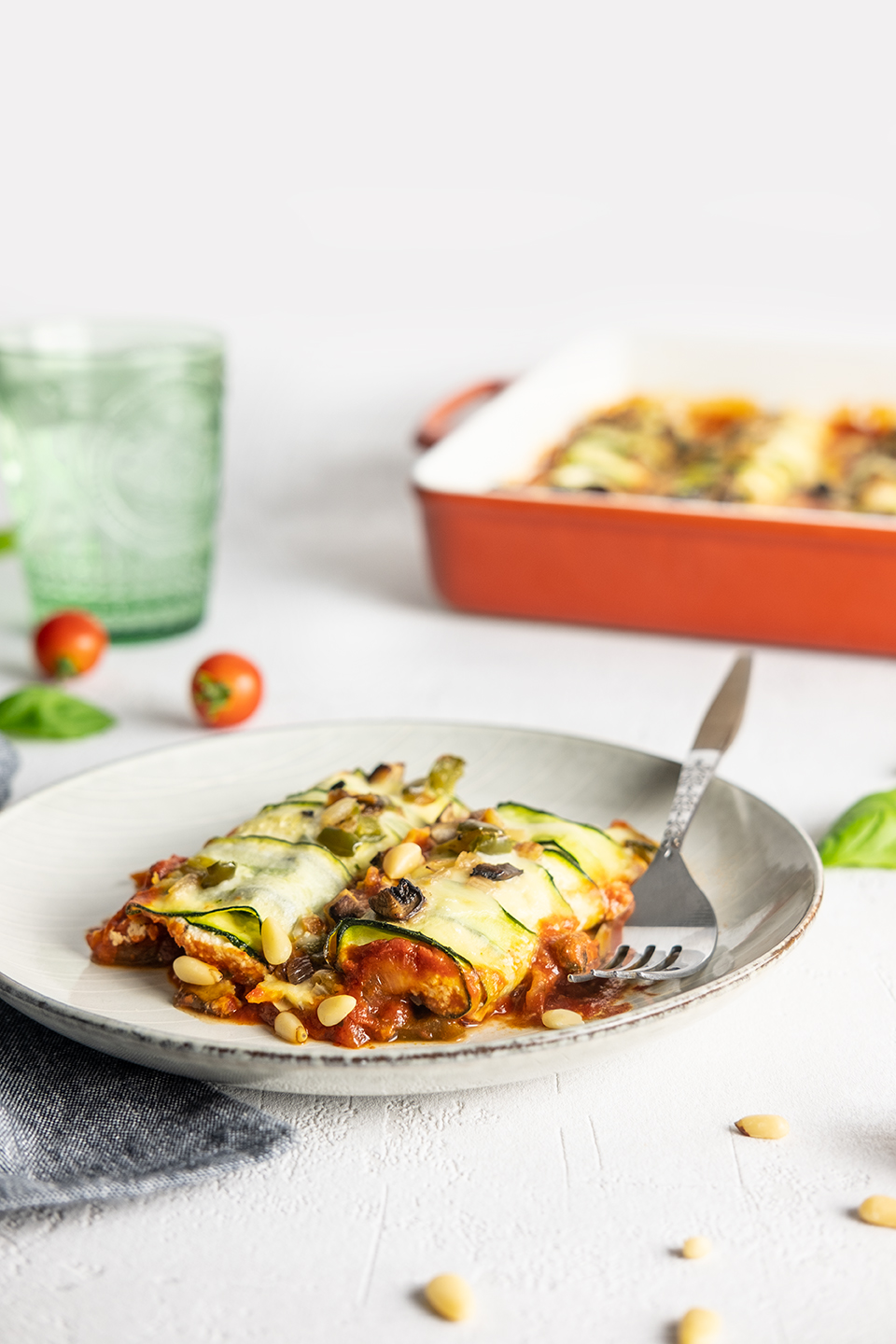  Two Low carb zucchini and ricotta cannelloni served on a grey salad plate.  Casserole dish in background with ice water in a green glass.  