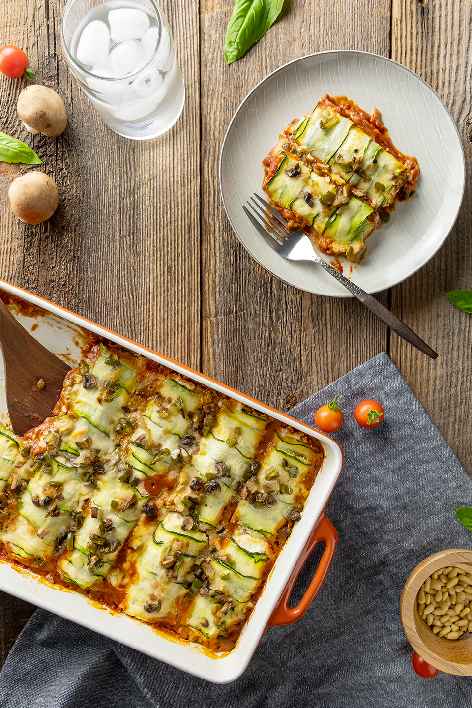  Low carb zucchini and ricotta cannelloni and grey plate with glass of ice water and mushrooms. 