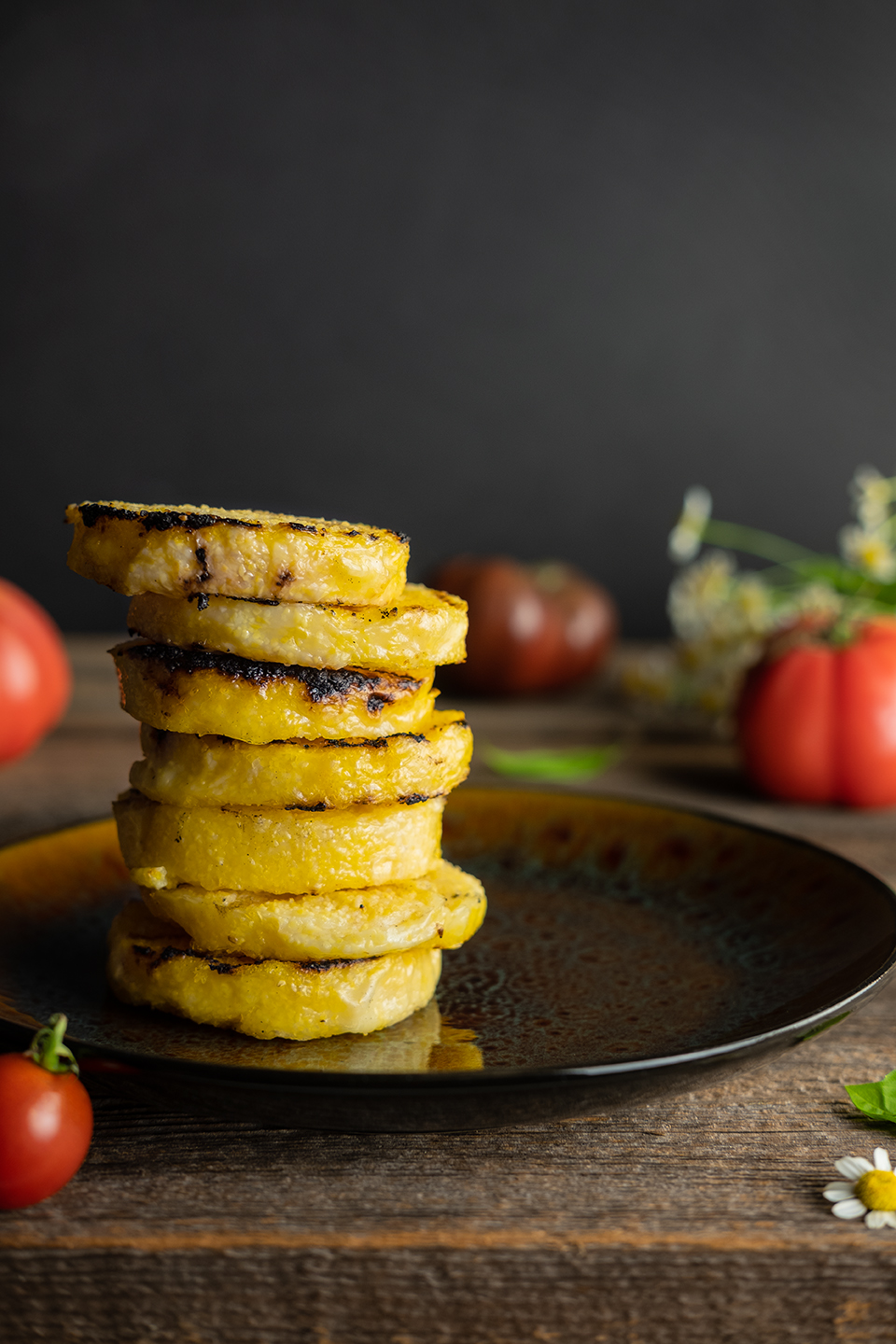  Grilled polenta on a wooden background stacked with tomatoes and basil. 