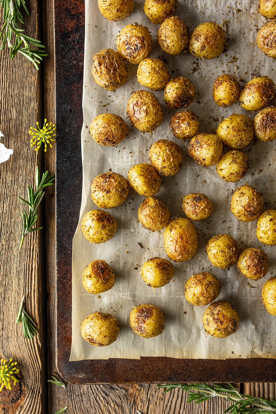  Rusty metal sheet pan with browned parchment paper on barn wood background.  Roasted baby potatoes with seasoning baked on the sheet pan. 